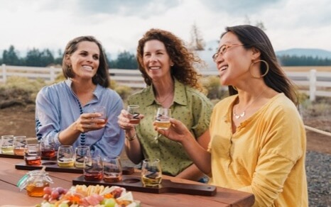 Three women enjoying wine tasting outdoors, surrounded by nature and a scenic view in Central Oregon.