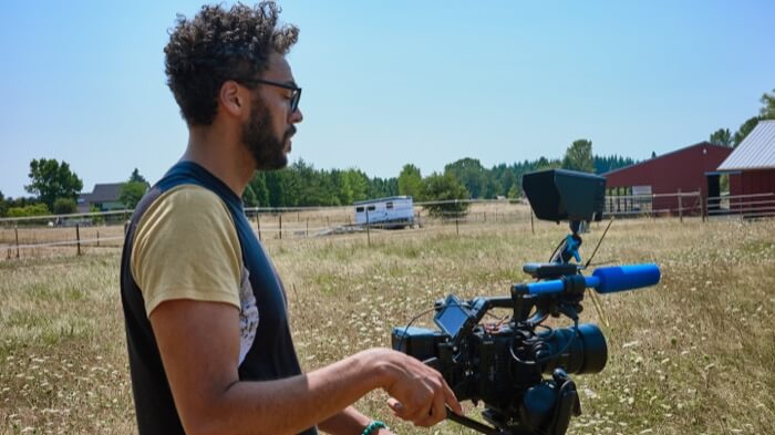 A filmmaker operates a professional camera in a grassy field, preparing to shoot a scene in Central Oregon.