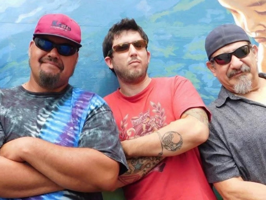 Three men with sunglasses and hats stand together in front of a colorful mural in Central Oregon.