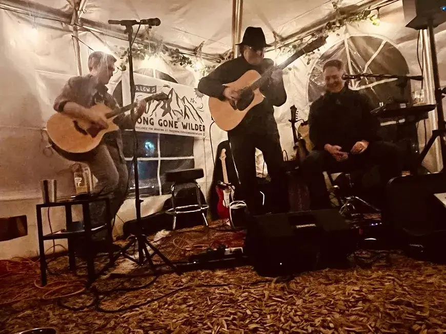 Three musicians perform an acoustic set in a cozy, tented venue with string lights and a rustic atmosphere in Central Oregon.