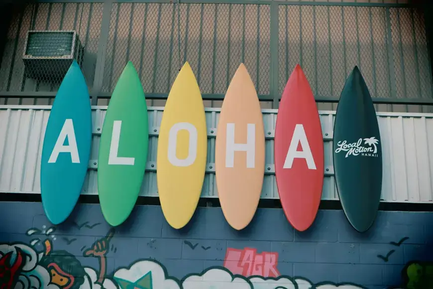 Five colorful surfboards spelling 'ALOHA' hang on a wall above vibrant graffiti in Central Oregon.