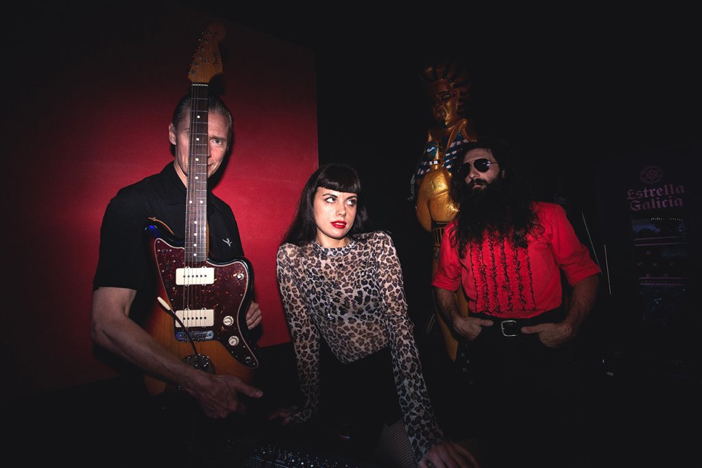 A musician with a guitar stands behind a woman in a leopard print top, with a bearded man in a red shirt to her right in Central Oregon.