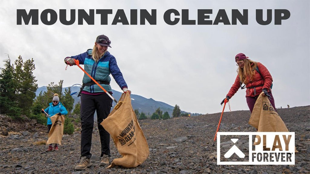 Volunteers in outdoor gear collect trash in a mountainous area using orange sticks and burlap bags in Central Oregon.