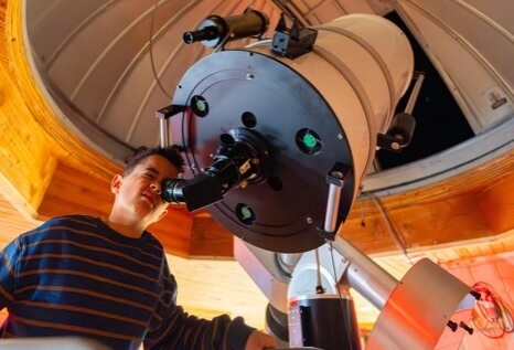 A young astronomer peers through a large telescope in a wooden observatory, gazing at the night sky in Central Oregon.