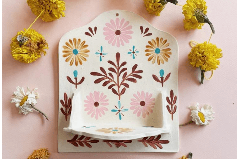 A decorative ceramic wall shelf adorned with colorful floral patterns and surrounded by dried yellow and white flowers in Central Oregon.