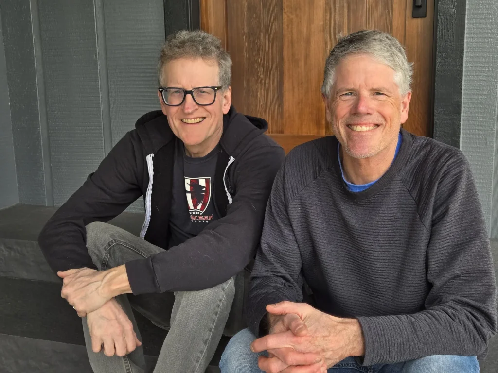 Two smiling men sitting on steps in front of a wooden door in Central Oregon.