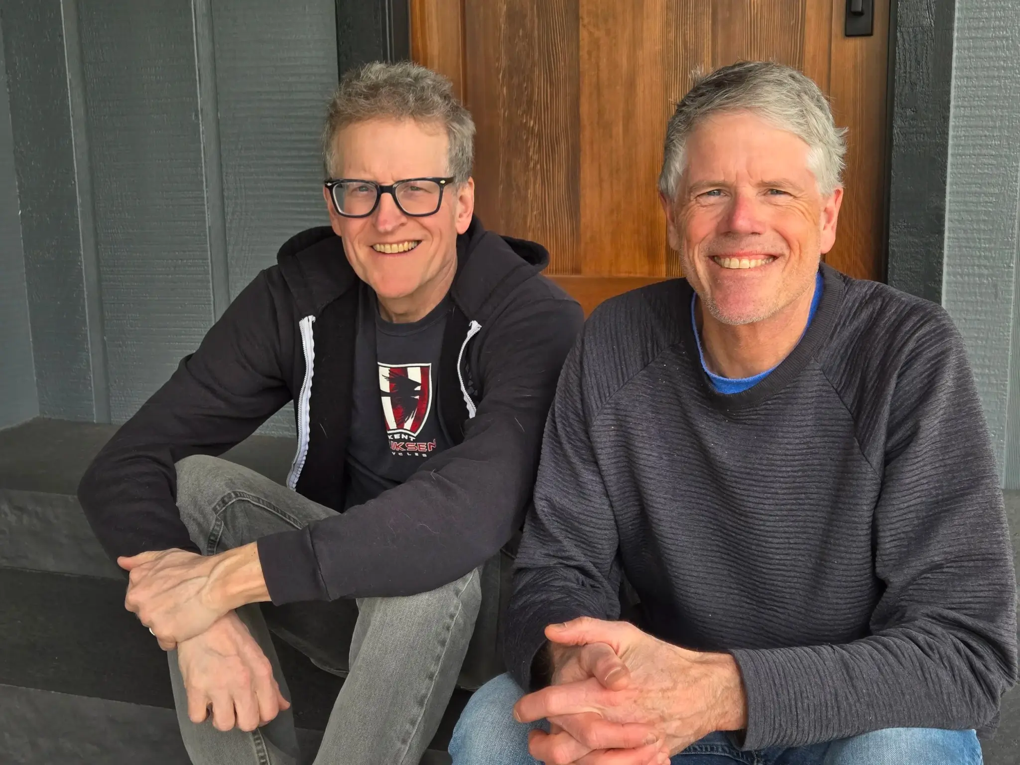 Two smiling men sitting on steps in front of a wooden door in Central Oregon.