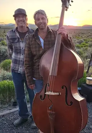 Two men stand in a desert landscape at sunset, one holding a double bass in Central Oregon.