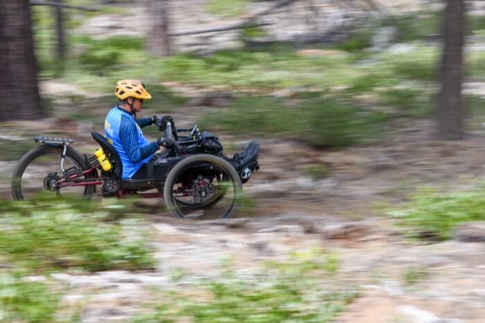 A person in a recumbent trike helmeted and wearing bright clothing rides through a wooded area in Central Oregon.