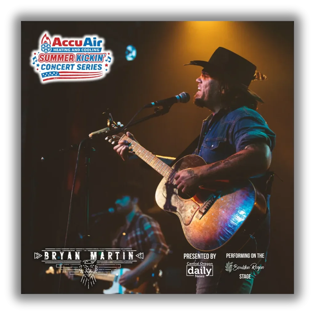 A musician wearing a cowboy hat passionately sings into a microphone while playing an acoustic guitar on stage in Central Oregon.
