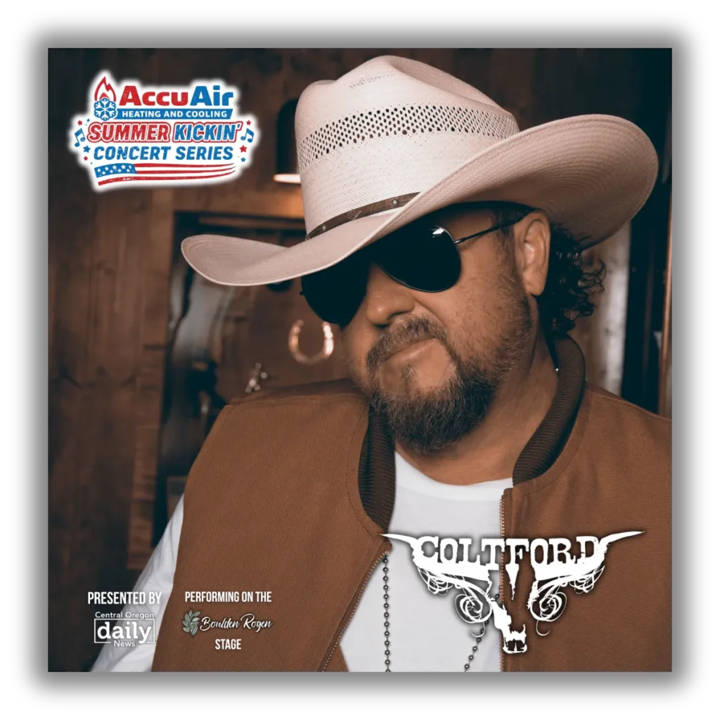 A man wearing a cowboy hat and sunglasses, with a beard, standing in front of a wooden background in Central Oregon.