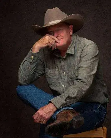 A man wearing a cowboy hat and denim shirt sits pensively on a stool in Central Oregon.