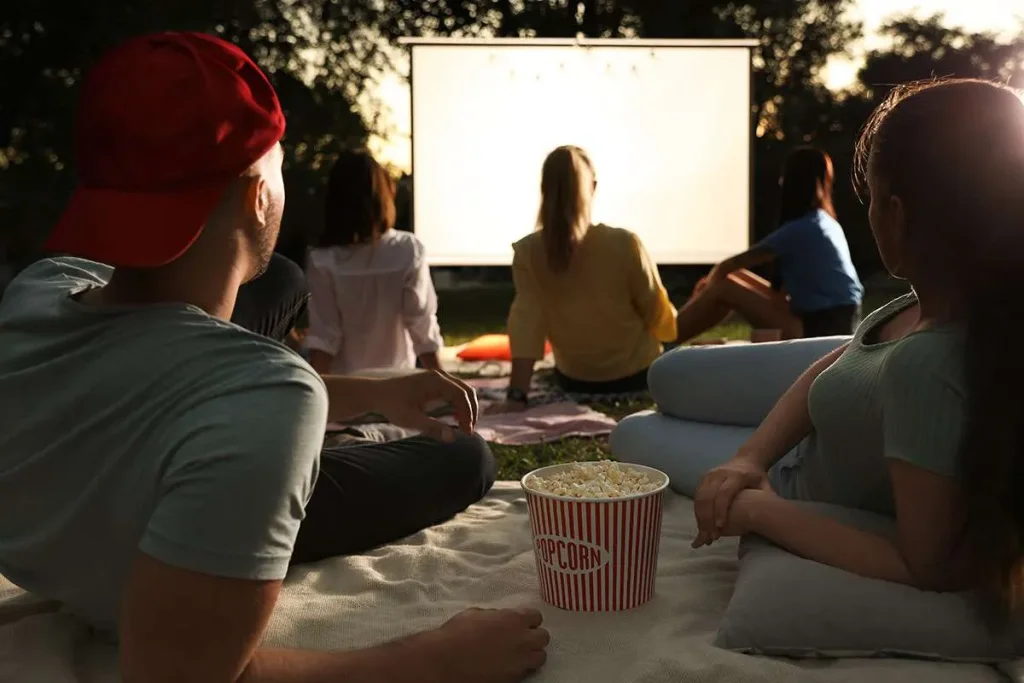 A group of friends enjoying an outdoor movie night, sitting on blankets with a large popcorn bucket, under the stars in Central Oregon.