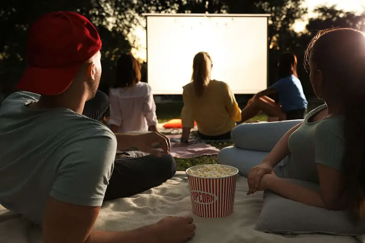 A group of friends enjoying an outdoor movie night, sitting on blankets with a large popcorn bucket, under the stars in Central Oregon.