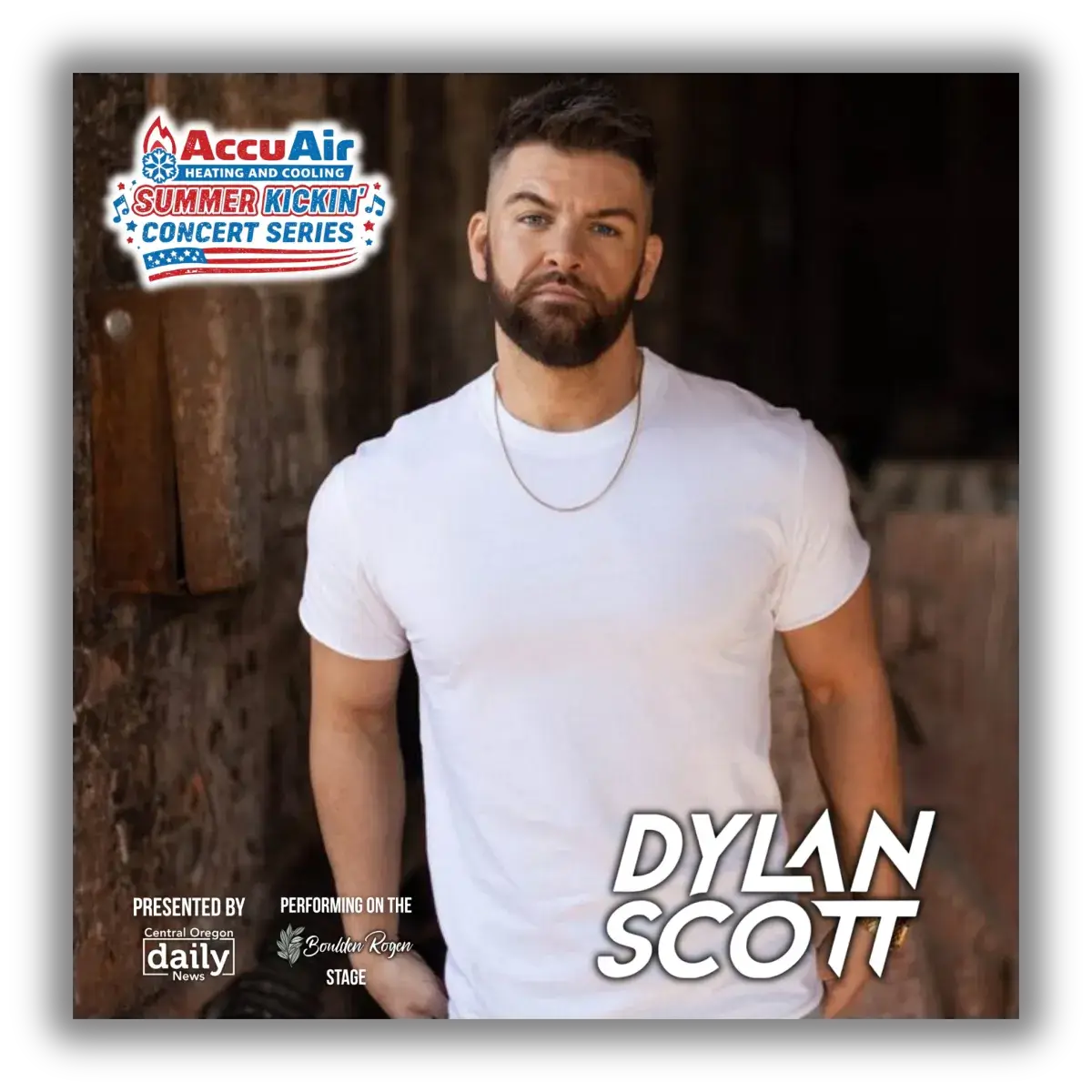 A muscular man with a beard wearing a white t-shirt stands confidently against a rustic brick wall in Central Oregon.