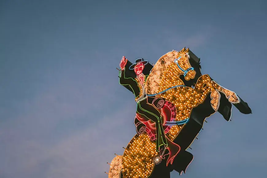 A vibrant neon sign depicts a cowboy riding a bucking bronco against a twilight sky in Central Oregon.