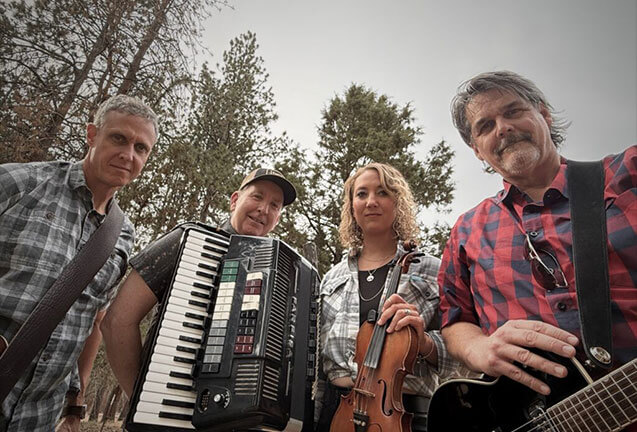 A group of four musicians playing an accordion, violin, and guitar outdoors among tall trees in Central Oregon.