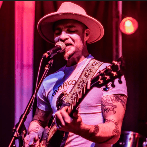A musician wearing a wide-brimmed hat and a light blue shirt performs on stage with an electric guitar in Central Oregon.