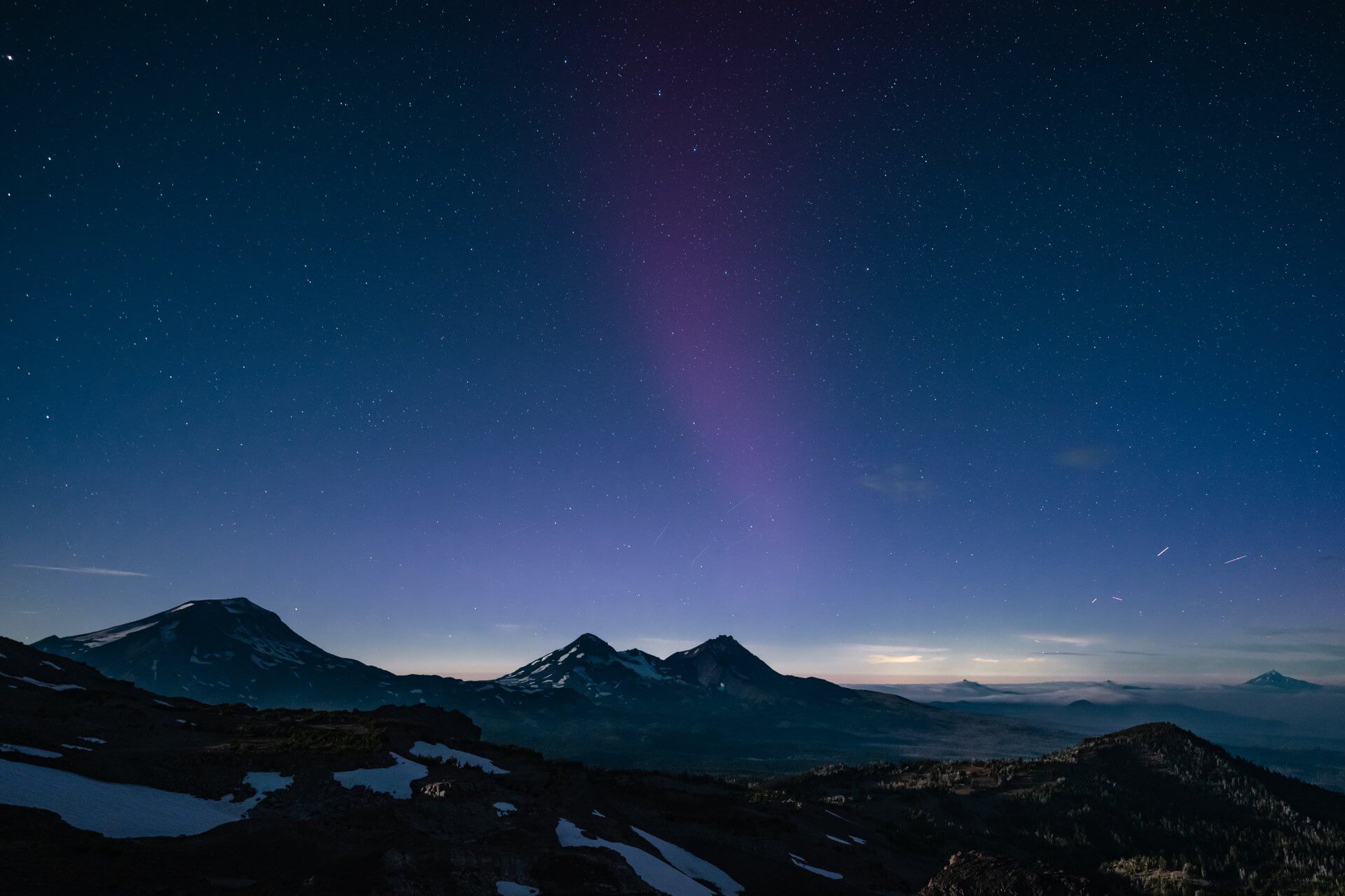 A breathtaking night sky over snow-capped mountains, illuminated by the Northern Lights and countless stars in Central Oregon.