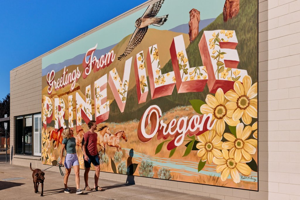 A vibrant mural welcomes visitors to Prineville, Oregon, with colorful horses, sunflowers, and a flying bird in Central Oregon.