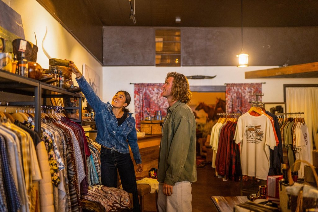 A couple enjoys browsing through a variety of clothing items in a cozy, dimly lit boutique in Central Oregon.