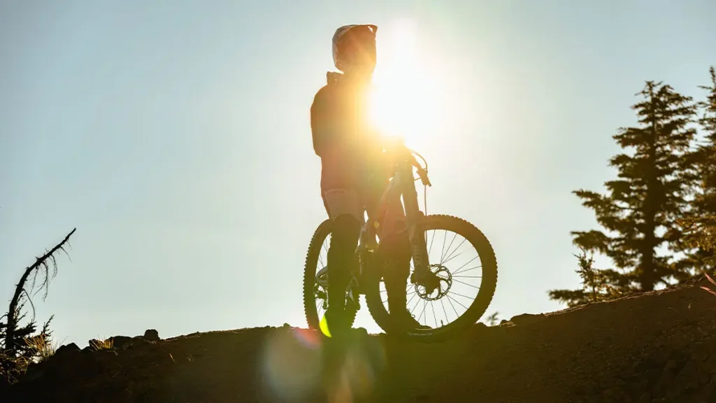 A cyclist stands silhouetted against the setting sun on a dirt trail, ready to ride into the evening in Central Oregon.