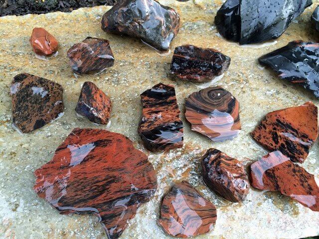 Various sizes of wet, dark red and black stones scattered on a light-colored rock surface in Central Oregon.