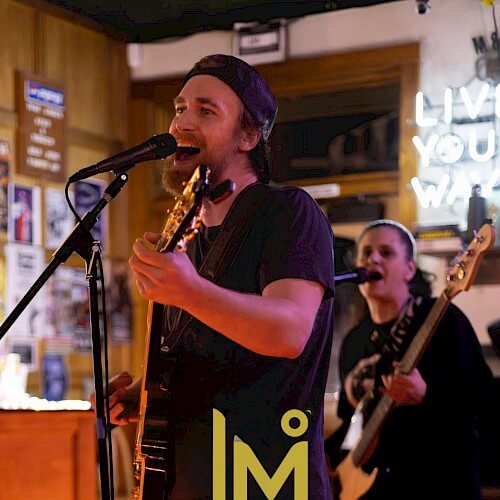A musician passionately singing and playing guitar on stage, accompanied by a bandmate in Central Oregon.