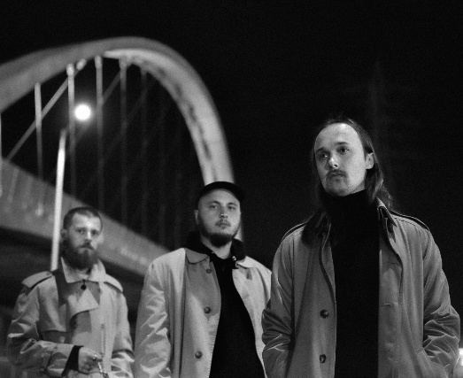 Three men in trench coats stand under a lit bridge at night in Central Oregon.