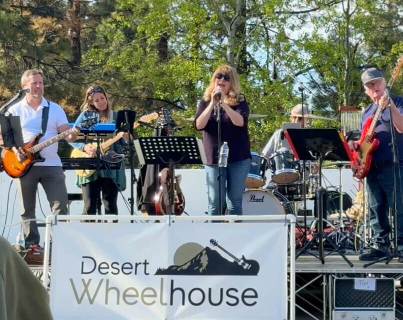 A band performs on stage at the Desert Wheelhouse outdoor concert venue, with a banner displaying the venue's name and logo in Central Oregon.