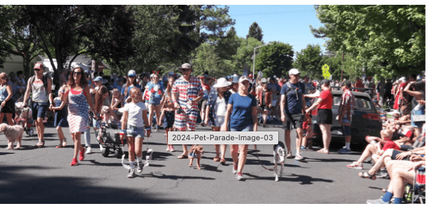 A lively pet parade featuring dogs and their owners dressed in patriotic attire, marching down a street lined with spectators in Central Oregon.
