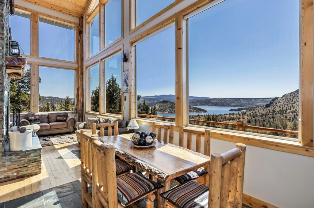 A spacious, rustic-modern cabin with expansive windows overlooking a serene lake and mountain range in Central Oregon.