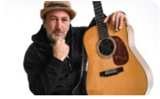 A man wearing a black hoodie and a hat is holding an acoustic guitar in Central Oregon.