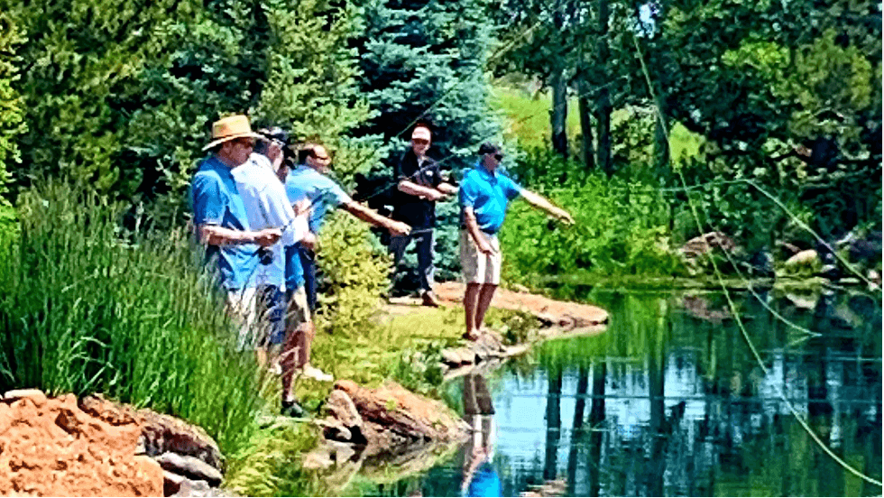 A group of people enjoying a sunny day fishing by a serene lake surrounded by lush greenery in Central Oregon.
