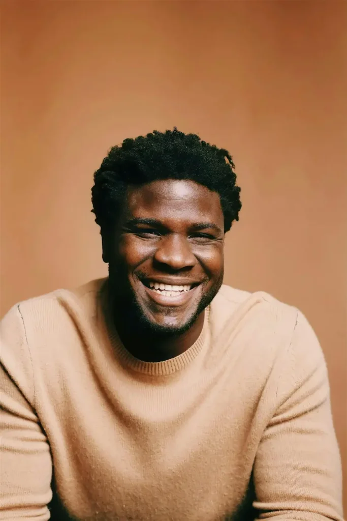 A man with a warm smile wearing a beige sweater against a soft orange background in Central Oregon.