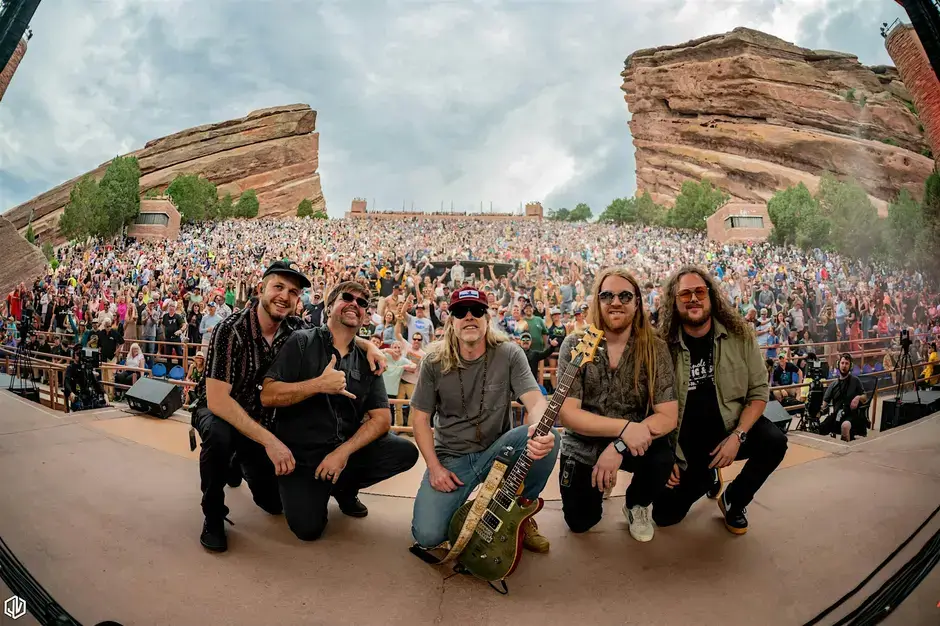 Four musicians pose on stage at Red Rocks Amphitheatre, surrounded by a massive crowd in Central Oregon.