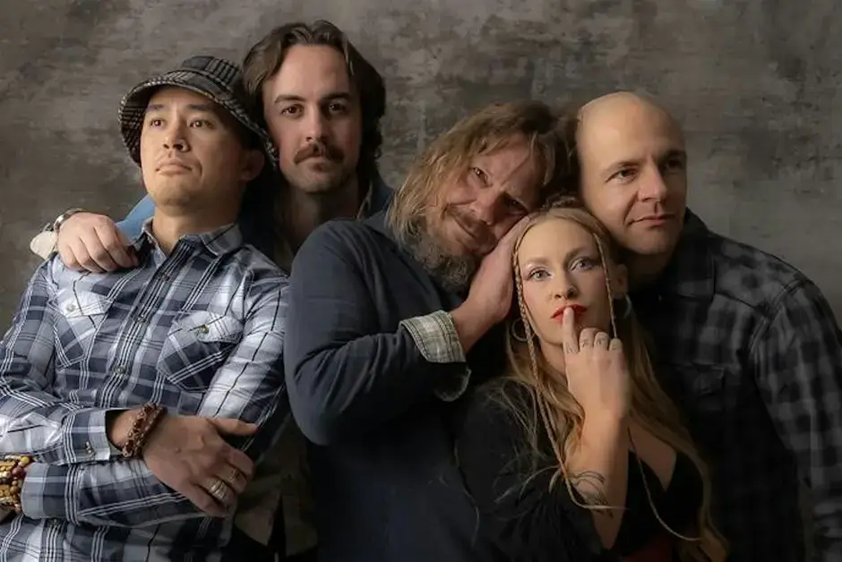 A group of five musicians pose together against a textured gray backdrop, showcasing their unique styles and personalities in Central Oregon.