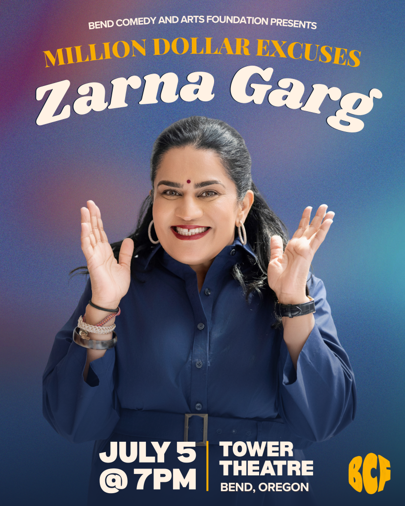 Zarna Garg, a woman with dark hair and a bindi, smiles broadly with her hands raised in excitement in Central Oregon.