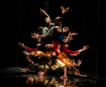 A dynamic dance performance featuring a group of dancers forming a human pyramid with outstretched arms, creating a visually striking and harmonious composition in Central Oregon.