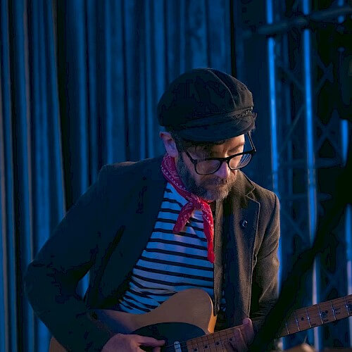 A musician wearing a beret and red bandana plays an electric guitar on stage in Central Oregon.