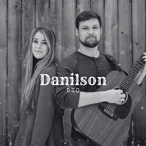 A black and white portrait of a man and woman standing close together, with the man holding an acoustic guitar in Central Oregon.