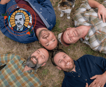 Four men and a cat are lying on their backs in a circle on a grassy field, smiling and looking up at the sky in Central Oregon.
