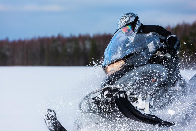 A snowmobiler in full gear speeds across a snowy landscape, kicking up a spray of snow in Central Oregon.