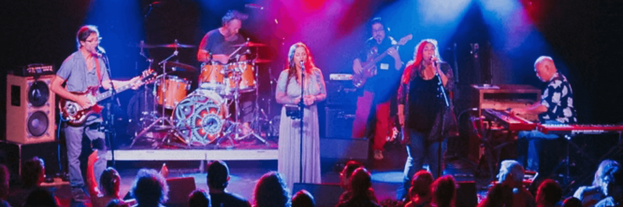 A vibrant live music performance featuring a band with guitars, drums, and keyboards, illuminated by colorful stage lights, as an enthusiastic audience watches from below in Central Oregon.