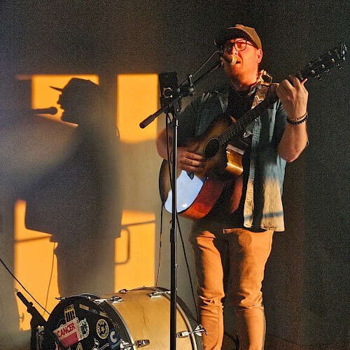 A musician performs an acoustic set in a dimly lit room, casting a shadow on the wall in Central Oregon.