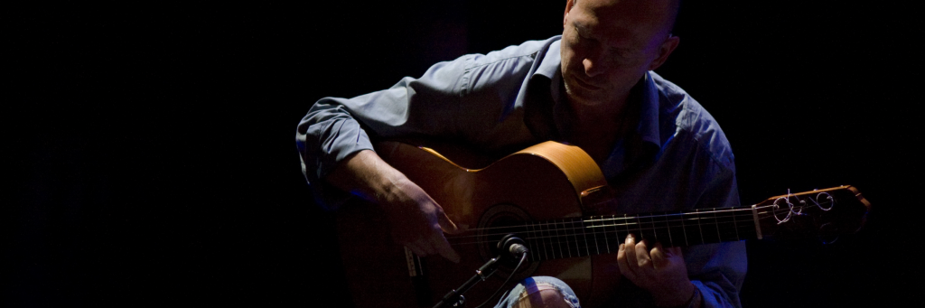 A musician deeply focused on playing an acoustic guitar in a dimly lit setting in Central Oregon.