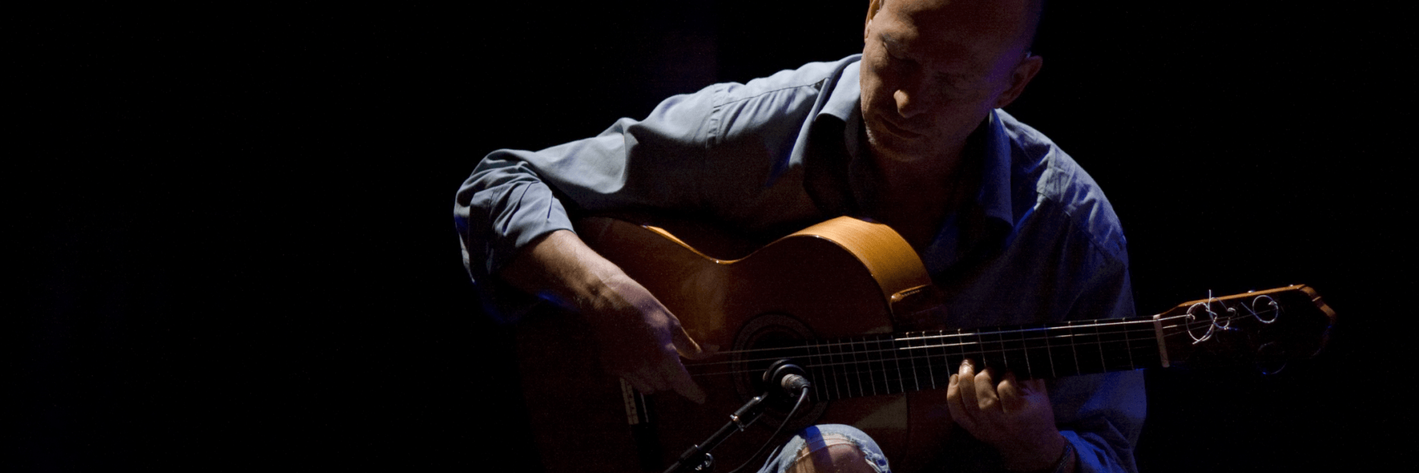 A musician deeply focused on playing an acoustic guitar in a dimly lit setting in Central Oregon.