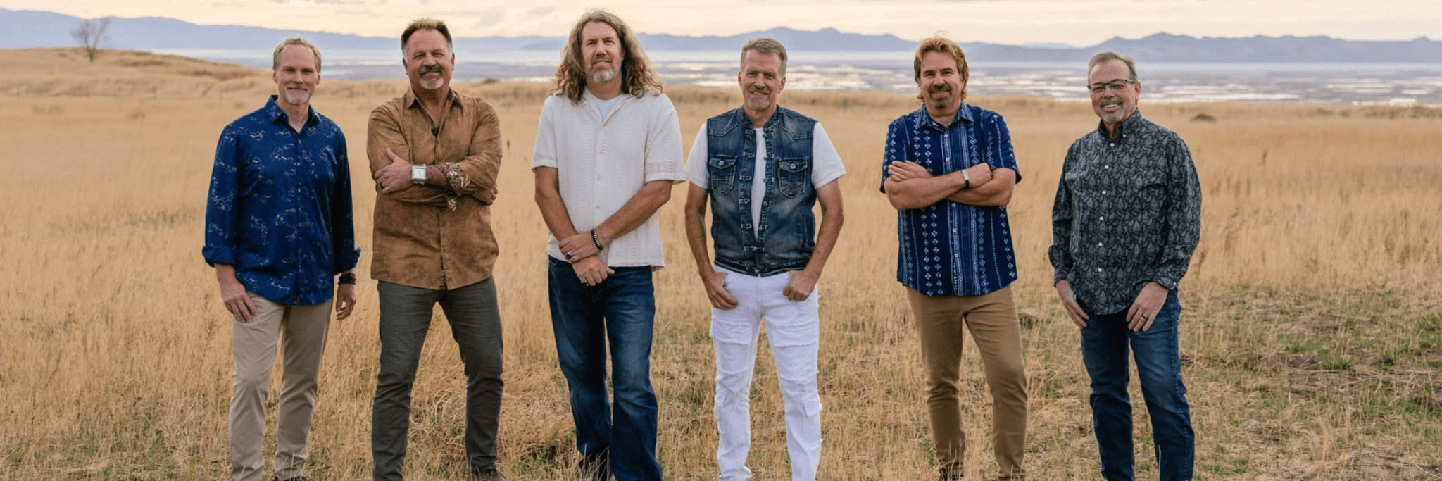 A group of five men standing in a field of tall, golden grass with mountains in the distance in Central Oregon.