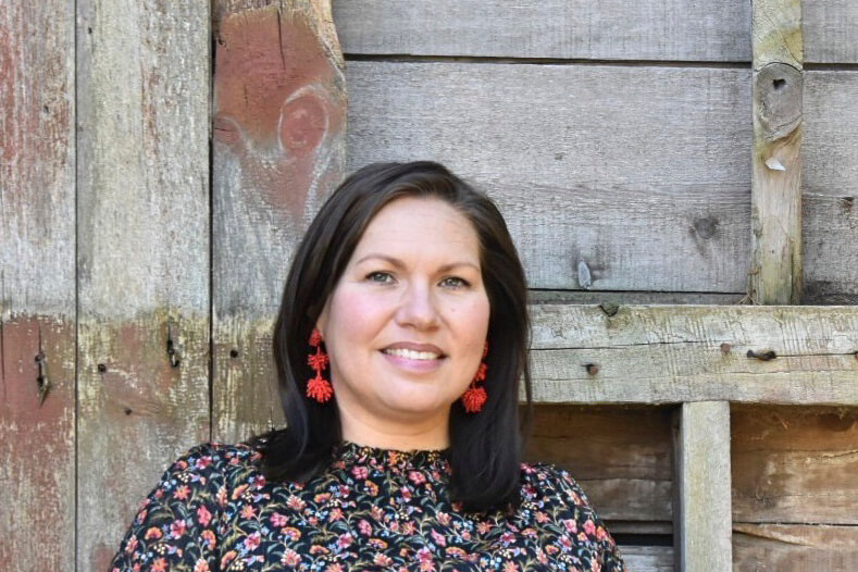 A smiling woman with dark hair wearing red tassel earrings and a floral top in Central Oregon.