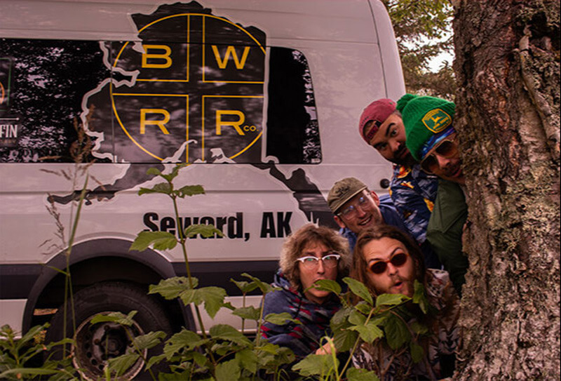 A group of friends peeking from behind a tree next to a van in Central Oregon.
